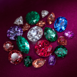 Multiple polished gemstones including diamonds, rubies, emeralds and sapphires